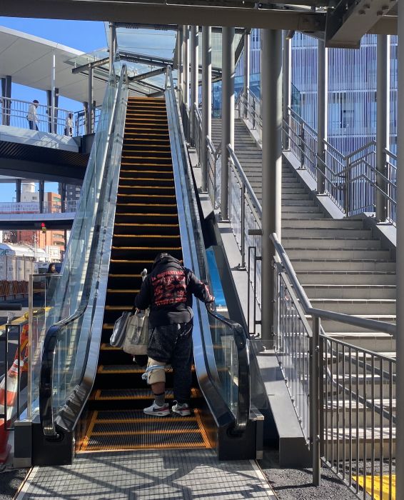 荷物を持ってエスカレーターで円形デッキに上る人