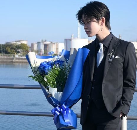 ブルーの花束を持ちコンビナートの前に立つ男性