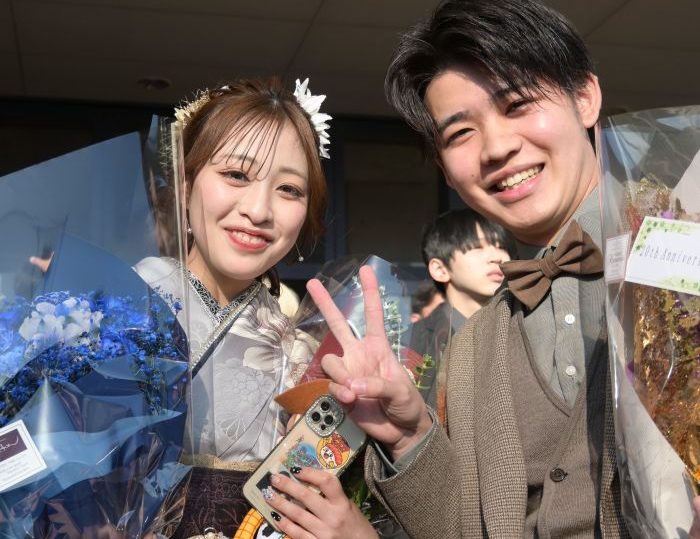 ウッディの人形とブルーのブーケを持つ女性と笑顔でピースする蝶ネクタイの男性