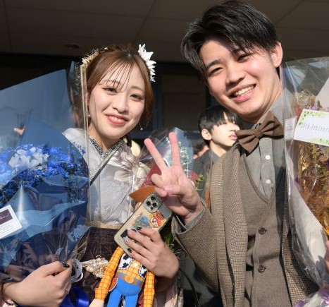 青を基調にしたブーケとトイストーリーのウッディの人形を手にする女性と、茶色の蝶ネクタイでピースをする男性